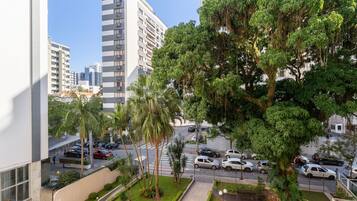 Un barrio residencial con un árbol grande, una calle con autos estacionados y edificios altos al fondo.
