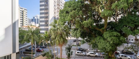 Un barrio residencial con un árbol grande, una calle con autos estacionados y edificios altos al fondo.