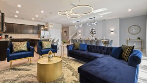 A modern living room with a blue sofa, a round coffee table, and a kitchen in the background. - Windsor Island 10br Waterpark Free (Davenport)