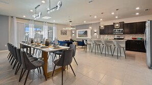 A modern kitchen with dark cabinets, a stainless steel refrigerator, and a dining area with a long table and chairs. - Windsor Island 10br Waterpark Free (Davenport)