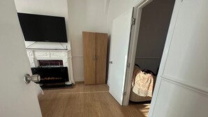 A room with a fireplace, a television mounted above it, a wooden wardrobe, and a door leading to another room.