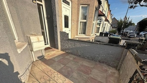 A residential street with a paved area in front of a house, a mailbox, and a door.