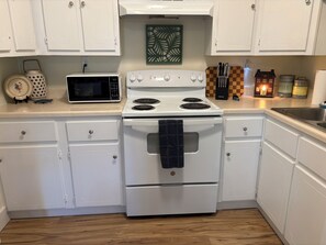 A kitchen with white cabinets, a microwave, a stove, and a checkered cutting board.