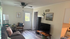 A living room with a sofa, armchair, TV, ceiling fan, and a door with a window. - Charming 2-bedroom barn-style home nestled on 6 acres in delightful Vienna (Vienna)