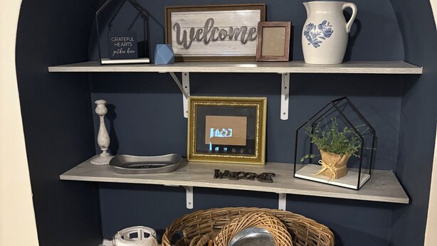 A dark blue arched wall with shelves displaying a welcome sign, a framed clock, a decorative pitcher, and a basket. - Charming 2-bedroom barn-style home nestled on 6 acres in delightful Vienna (Vienna)
