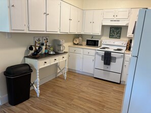 A kitchen with white cabinets, a microwave, a coffee maker, and a trash bin.
