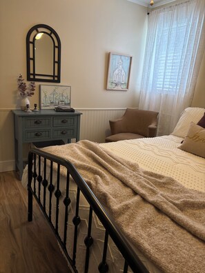 A bedroom with a bed, a dresser, a mirror, a painting, and a window with curtains.