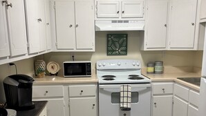 A kitchen with white cabinets, a white stove, a microwave, and a coffee maker. - Charming 2-bedroom barn-style home nestled on 6 acres in delightful Vienna (Vienna)