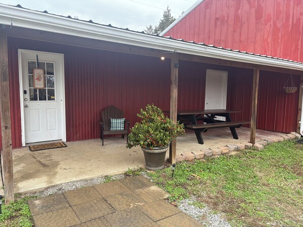 A red barn with a white door, a bench, and a potted plant on the porch.