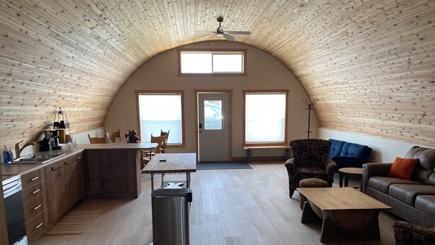 Un loft amplio con techo alto, paredes de madera, zona de cocina, mesa de comedor y área de estar con sofá y sillones.