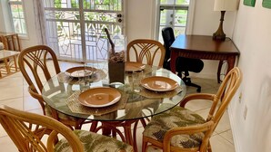 Comedor con mesa de vidrio rodeada de sillas de mimbre con cojines de hojas de palma.