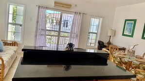 Una habitación con un piano, una mesa de comedor con sillas y vistas amplias por los ventanales.