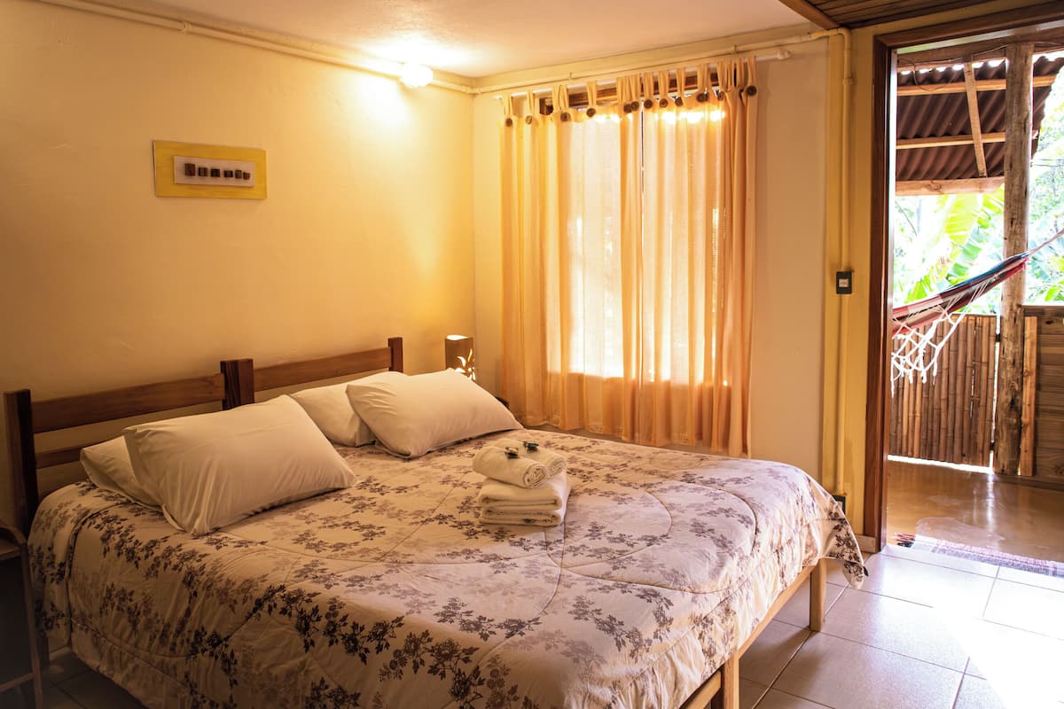 A neatly made bed with a floral bedspread and pillows, a bedside lamp, and a window with curtains.