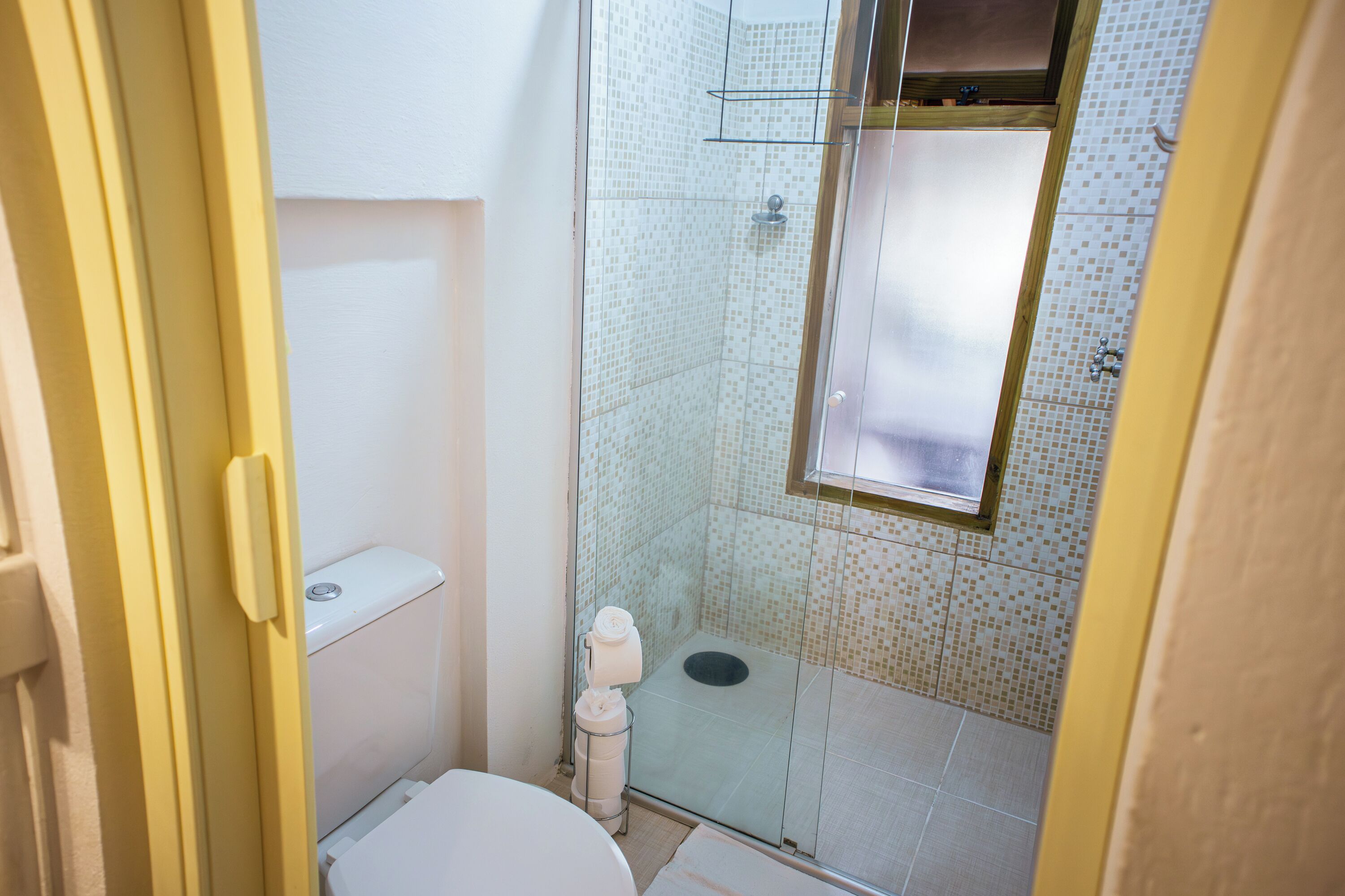A small bathroom with a toilet, a glass shower enclosure, and a tiled floor.