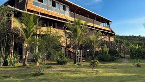 A two-story wooden building with large windows and a balcony, surrounded by lush greenery and a clear sky. - Espaço Flor das Águas  (Cunha)