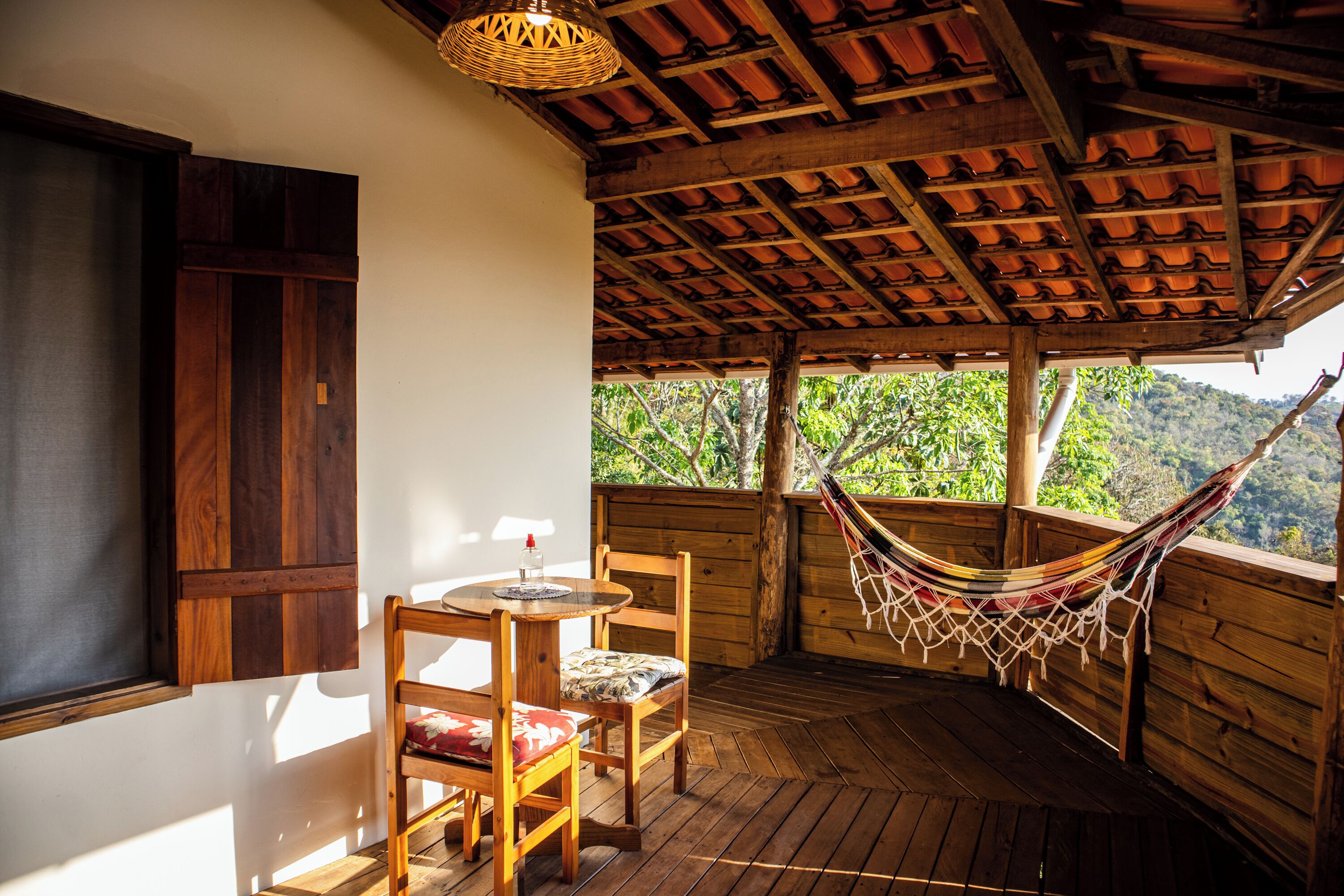 A wooden deck with a table and chairs, a hammock, and a view of greenery.