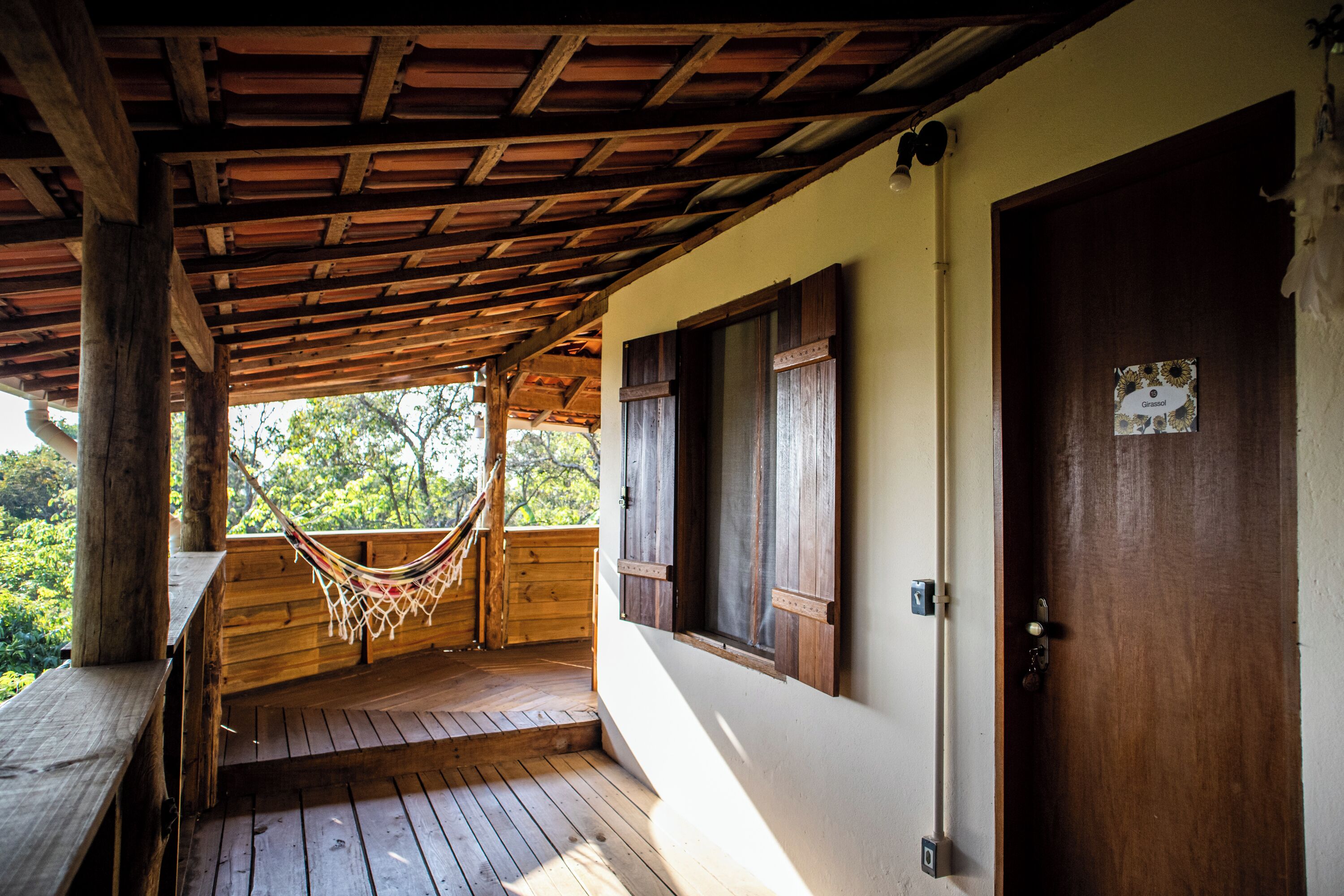 A wooden porch with a hammock, wooden benches, and a door with a sign.