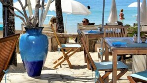 Een terras met houten tafels en stoelen, een grote blauwe vaas en parasols voor schaduw.
