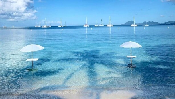 Een rustige zee met zeilboten en twee witte parasols op het water.