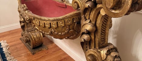 An ornate, gold-accented chair with a red cushioned seat, positioned on a wooden floor with a patterned rug.