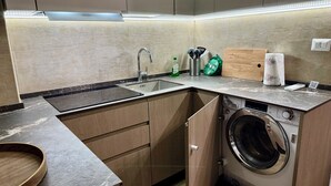 Een kleine keuken met een ingebouwde wasmachine, een spoelbak en een houten snijplank.
