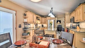 A modern kitchen with wooden cabinets, a stainless steel refrigerator, and a dining area set for four. - Family-Friendly Home w/ Hot Tub: 1 Mile to Downtown (Estes Park)
