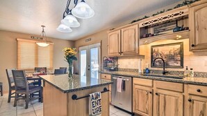 A kitchen with wooden cabinets, granite countertops, a central island, and a dining area with chairs and a table. - Family-Friendly Home w/ Hot Tub: 1 Mile to Downtown (Estes Park)