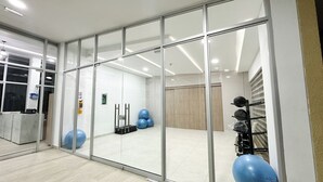 A modern fitness room with glass walls, exercise equipment, and a reception area. - Mar Serena Beachside Stay  (Cartagena)