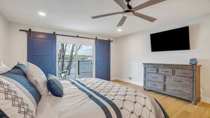 A bedroom with a bed, a dresser, a ceiling fan, and a TV mounted on the wall. - Waterfront Elegance: Spacious 5BR Lake Home with Game Room & Private Dock Access (Osage Beach)