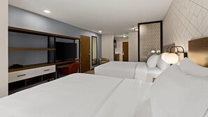 Ein Hotelzimmer mit zwei Betten, einem Fernseher, einem Schreibtisch und einem Sessel.
