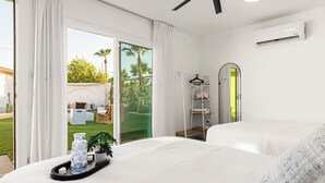 A modern hotel room with two beds, a large sliding glass door to a patio, and a white air conditioning unit.