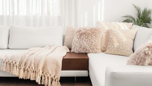 A modern living room with a white sofa, a wooden side table, and a beige throw blanket.