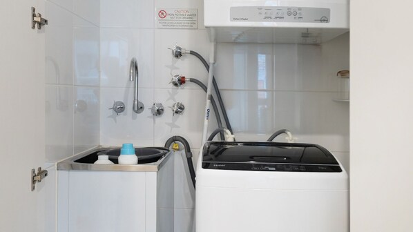 Un baño moderno con lavadora y secadora integradas, un lavamanos con una botella de jabón y un letrero de precaución sobre el agua no potable.
