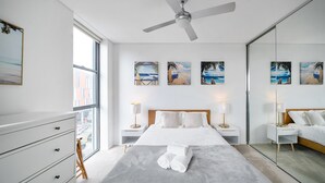 A modern bedroom with a large bed, bedside tables, a ceiling fan, and beach-themed wall art.