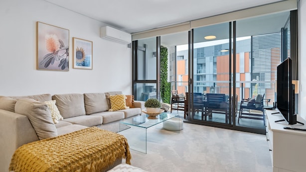 A modern living room with a sofa, coffee table, and a view of the city through large windows.