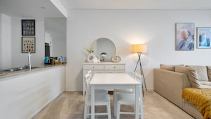 A modern kitchen with white cabinetry, a dining table with chairs, a large mirror, and a floor lamp.