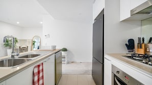 A modern kitchen with stainless steel appliances, a built-in oven, and a microwave. There is a sink with a faucet, a countertop with a plant, and a wooden cutting board.