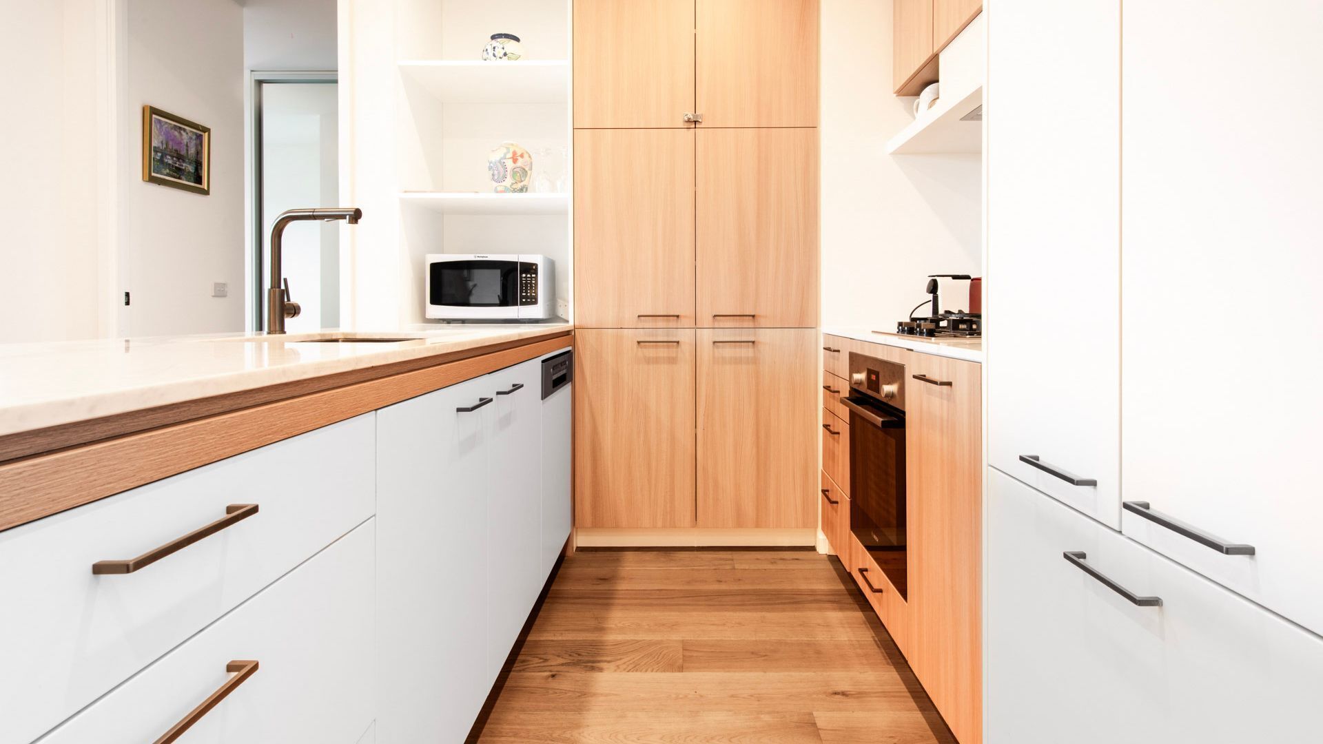A modern kitchen with white cabinetry, a wooden countertop, a microwave, and a stove.