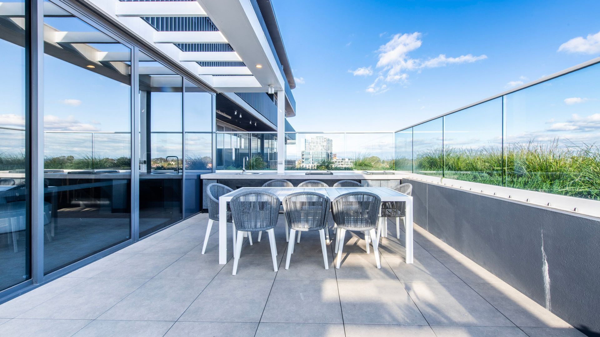 Une terrasse sur le toit, avec une table et des chaises, des murs en verre et une vue sur le paysage urbain.