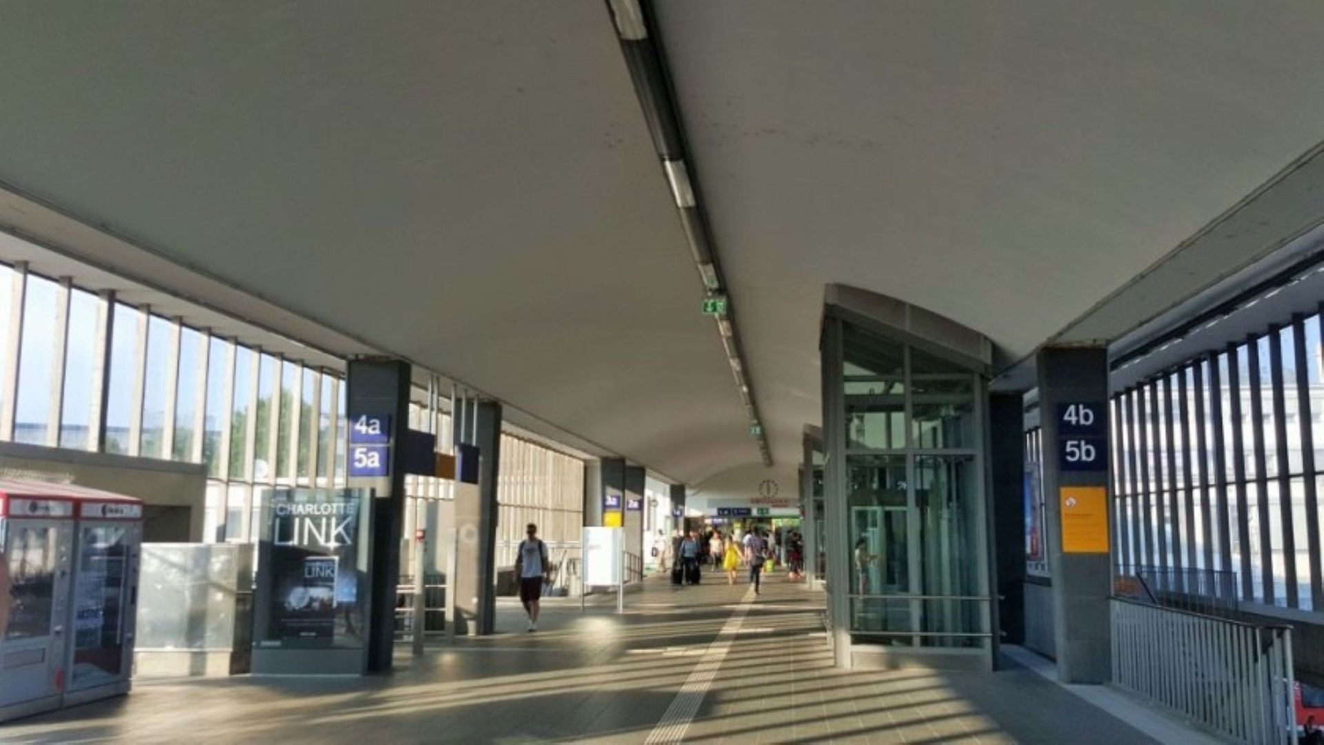 A spacious indoor area with directional signs for different zones, a bus stop, and a glass entrance.