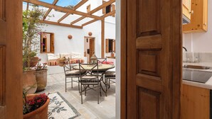 An open-plan living area with a wooden ceiling, a dining table with chairs, a sofa, and a kitchen area with wooden cabinets and a sink. - Villa Vasoula Lindos  (Lindos)