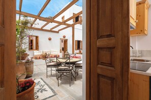 An open-plan living area with a wooden ceiling, a dining table with chairs, a sofa, and a kitchen area with wooden cabinets and a sink. - Villa Vasoula Lindos  (Lindos)