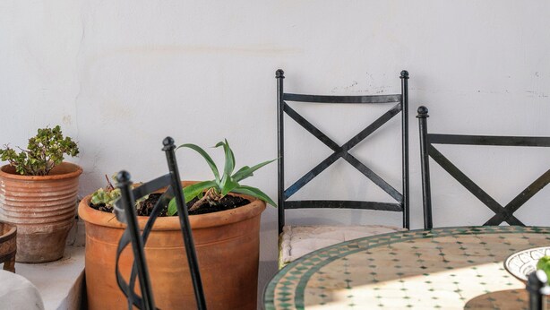 A wooden door with glass panels, a round table with a patterned tablecloth, and two potted plants. - Villa Vasoula Lindos  (Lindos)