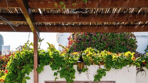 A brown door with a metal handle, a potted plant to the left, and a small table with a plate and two cups to the right. - Villa Vasoula Lindos  (Lindos)