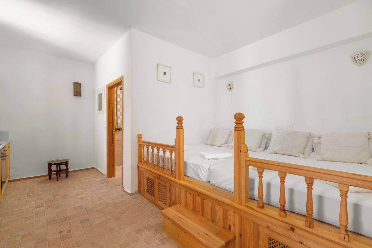 A bedroom with a wooden staircase, a bed with white bedding, and a small wooden stool.