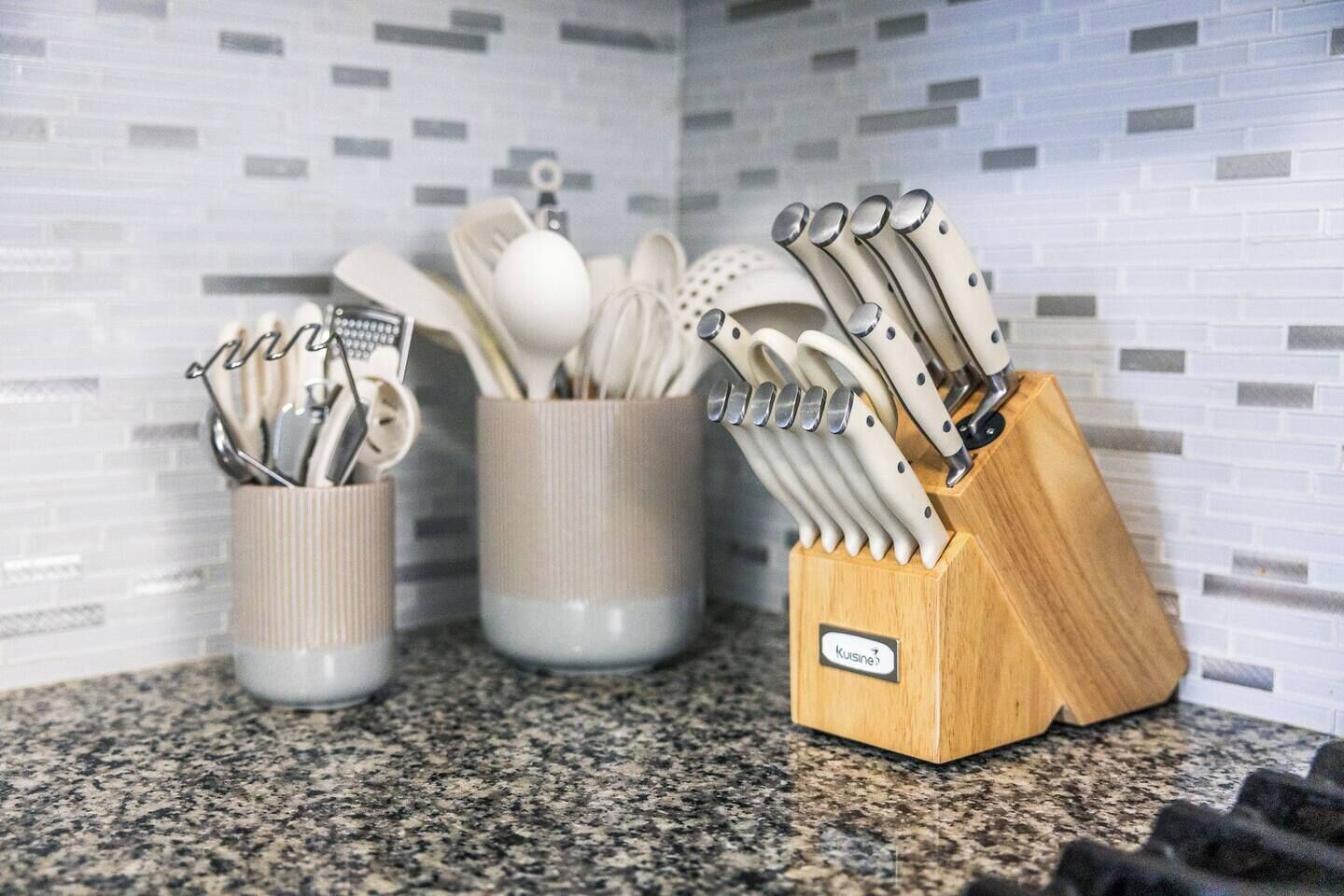 Una encimera de cocina con tres soportes para utensilios que contienen diversas herramientas de cocina.