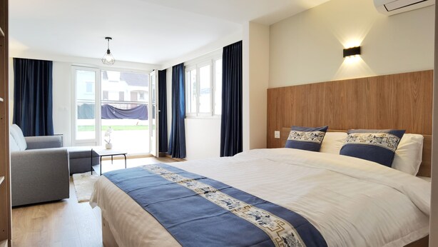 Een moderne hotelkamer met een groot bed, een sofa en een kleine tafel. Er is een balkon met gordijnen en uitzicht op buiten.