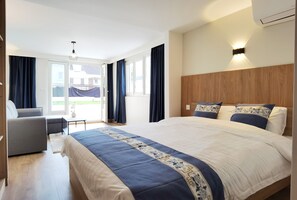 Ein modernes Hotelzimmer mit einem großen Bett, einer Couch und einem kleinen Tisch. Ein Balkon mit Vorhängen bietet Blick ins Freie.