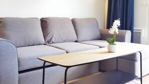 Een moderne woonkamer met een grijze bank, een houten salontafel en een wandlamp.