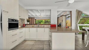 A modern kitchen with white cabinets, a built-in oven, and a large island with a red countertop. - Beachfront 7 Penthouse (Sawtell)